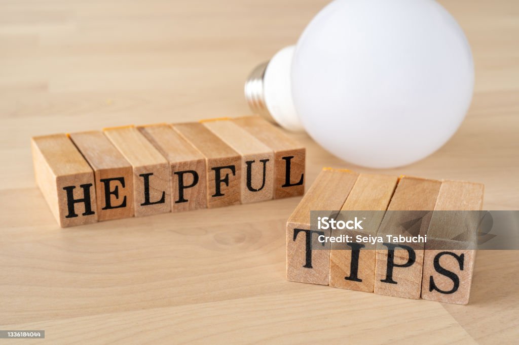 HELPFUL TIPS; Wooden stamps with "HELPFUL TIPS" text of concept and a light bulb on the table. Advice Stock Photo