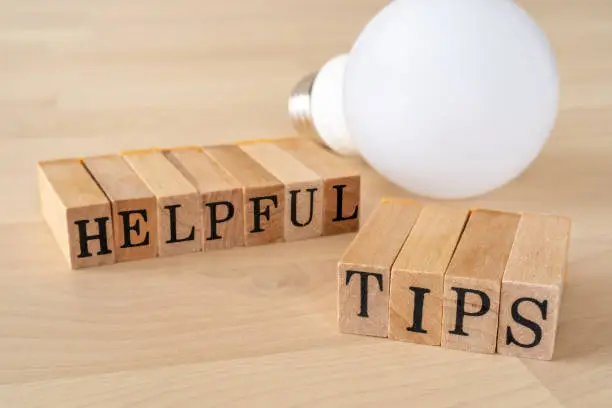 HELPFUL TIPS; Wooden stamps with "HELPFUL TIPS" text of concept and a light bulb on the table.