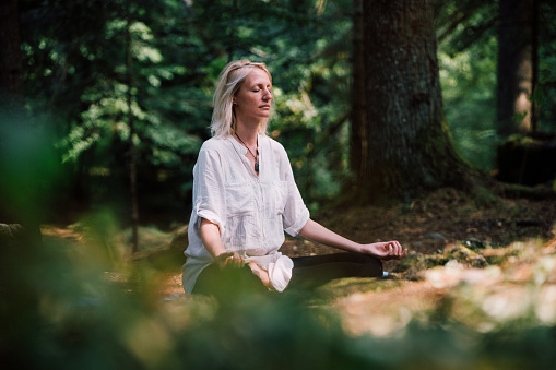 Beautiful young woman with long blonde hair meditates in nature, in a beautiful field. Travel and healthy lifestyle, enjoying nature