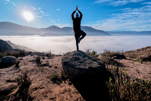 silhouette of a young person doing yoga on the mountain in sunrise over the clouds