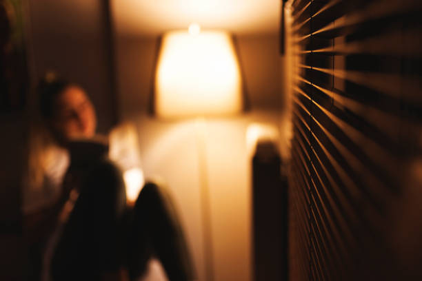 young woman alone at home reading a book in dim light