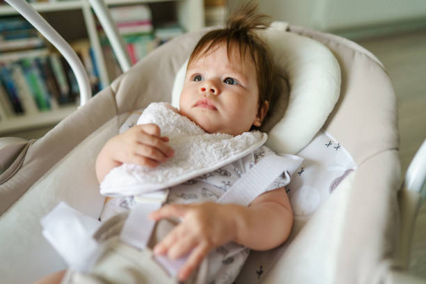 portrait del bebé caucásico pequeño que miente en la horquilla del asiento del columpio en sitio brillante en día en el hogar que mira al espacio lateral de la copia - swing rocker fotografías e imágenes de stock