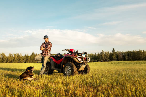 Farmer with is quadbike and dog on farm field Farmer standing by his quad bike looking at the dog sitting in front on the field on a summer day quadbike photos stock pictures, royalty-free photos & images