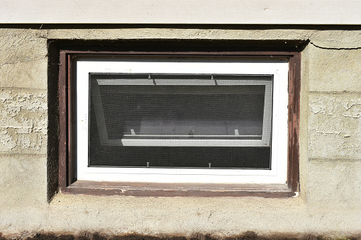 An image of an old basement window with brown painted trim.