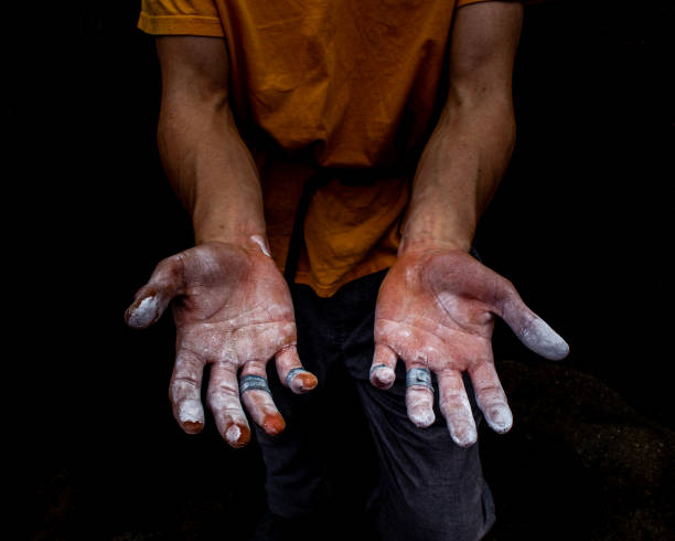 Close-up of a person applying chalk to their hand in preparation for weightlifting, emphasizing grip and readiness in a gym setting with fitness equipment visible.