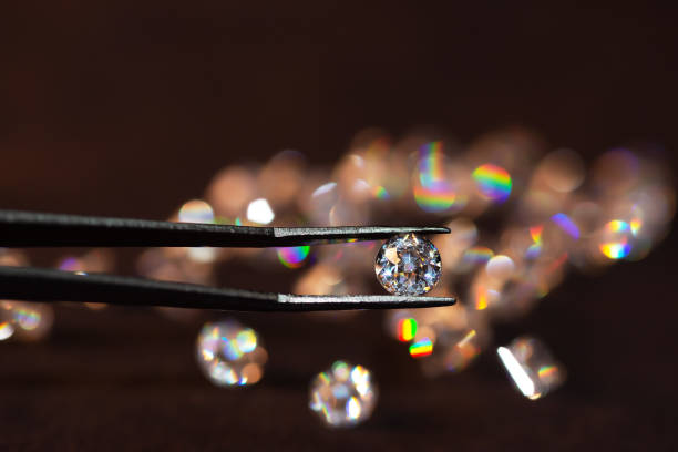 Diamond in tweezers on a dark background with diamonds group soft focusing Diamond in tweezers on a dark background with diamonds group soft focusing facet joint photos stock pictures, royalty-free photos & images