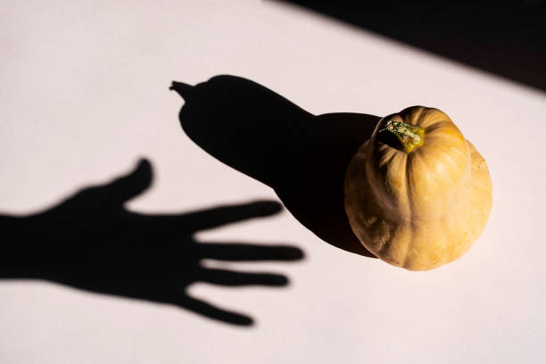 istock Hand silhouette reaching for Halloween pumpkin, creative composition with shadows. Mockup leaflet or flyer in minimalism style. 1336212929