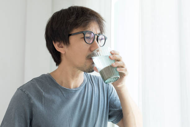 istock Asian man drinking water while standing by window at home. 1336215423