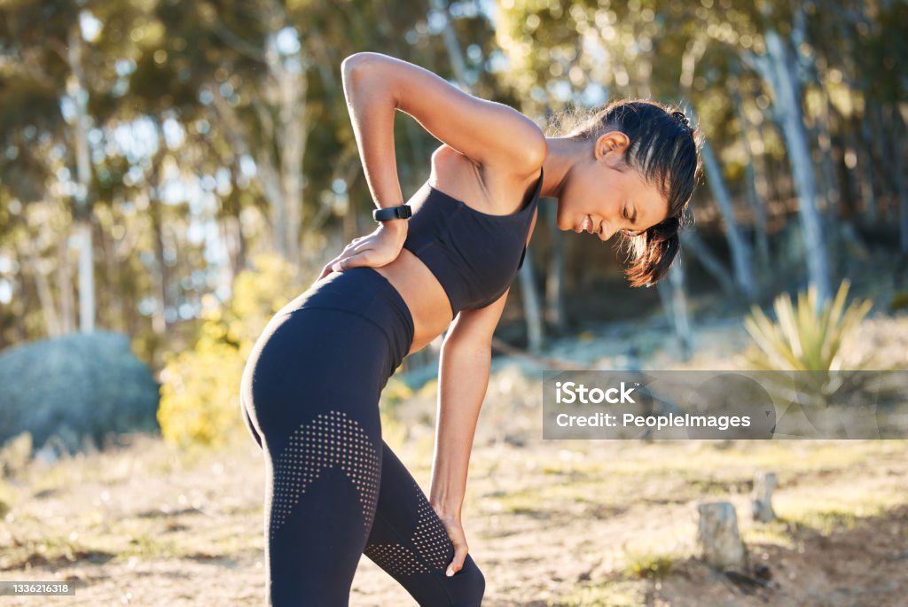 Shot of a young woman experiencing back pain while working out in nature Back ache is such a buzz kill Backache Stock Photo