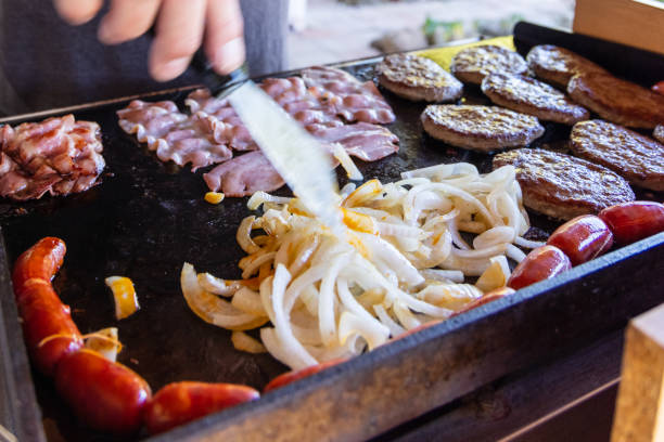 Meat on a iron griddle gas BBQ Preparing hamburgers, sausage, bacon, onions on a iron griddle on a gas BBQ spanish hamburger stock pictures, royalty-free photos & images