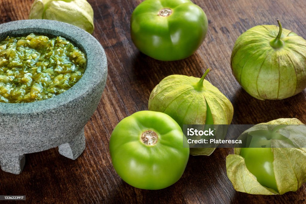 Tomatillos, green tomatoes, with salsa verde, green sauce, in a molcajete Tomatillos, green tomatoes, with salsa verde, green sauce, in a molcajete, traditional Mexican mortar, on a dark rustic wooden background Tomatillo Stock Photo