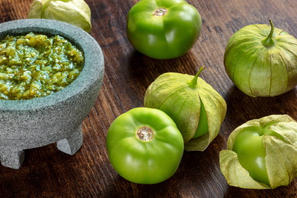 Tomatillos, green tomatoes, with salsa verde, green sauce, in a molcajete Tomatillos, green tomatoes, with salsa verde, green sauce, in a molcajete, traditional Mexican mortar, on a dark rustic wooden background tomatillo photos stock pictures, royalty-free photos & images