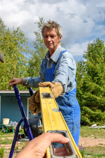 istock Male worker in a construction uniform takes a construction level from his hands at a street construction site. Construction of a pavilion, pergola near a country house on a summer day 1336224502