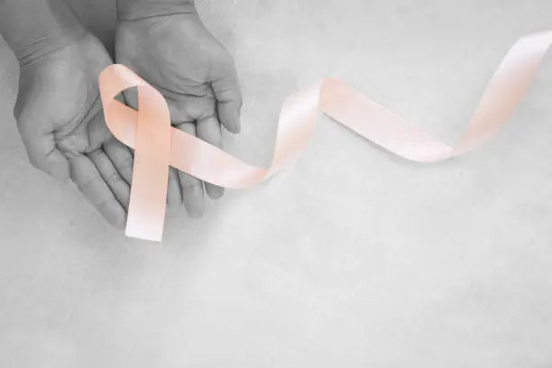 Hand holding Peach color ribbon curl on white fabric background with copy space, symbol for Uterine and Endometrial cancer awareness, World Cancer Day. Healthcare or hospital and insurance concept.