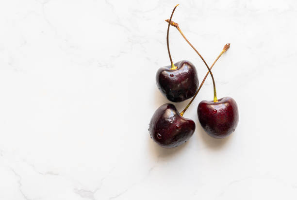 istock Top view fresh red cherries on marble floor, flat lay design, group of three fresh red cherries, small water drop on the fruit. 1336228114