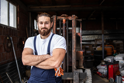 One man, a car mechanic, is in a car repair shop repairing a crane that makes it easier to work in a warehouse.