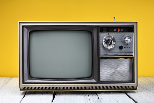 An old vintage television set from the 1970s stands on a wooden table against a yellow background. Vintage TVs 1980s 1990s 2000s.