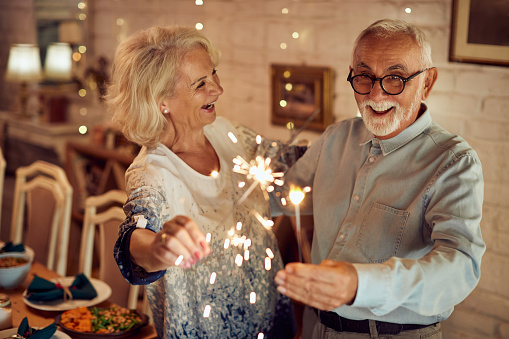 Feliz pareja de ancianos divirtiéndose con bengalas mientras celebra la Navidad en casa. photo