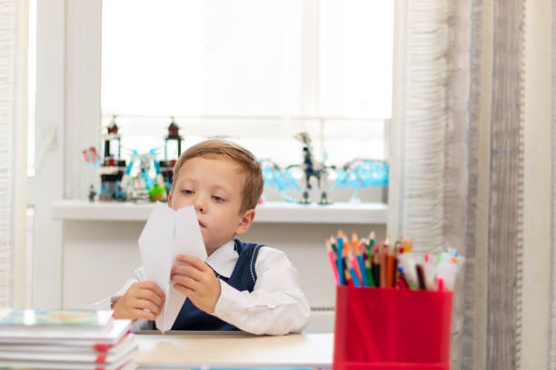 istock A cute first-grader boy in a school uniform at home while isolated at his desk makes a paper airplane during recess. Selective focus 1336231463