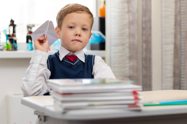 istock A cute first-grader boy in a school uniform at home while isolated at his desk makes a paper airplane during recess. Selective focus 1336231472