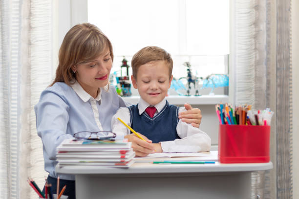 istock A beautiful young mother with her son is doing homework at a desk at home against a light background of a window during a pandemic quarantine. Selective focus 1336231507