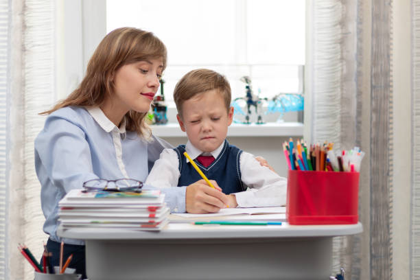 istock A beautiful young mother with her son is doing homework at a desk at home against a light background of a window during a pandemic quarantine. Selective focus 1336231509