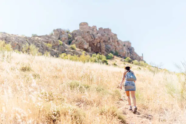 Photo of Woman ascending a hill towards a medieval castle.