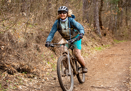Young mountain biker covered by mud riding down a forest trail