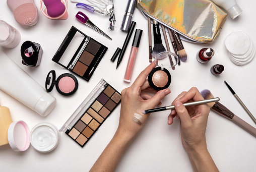 Top view of woman holding eyeshadow on hands over white table with cosmetic products. Decorative cosmetics and makeup brushes