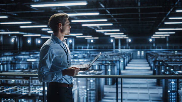 istock Portrait of IT Specialist Uses Laptop in Data Center. Server Farm Cloud Computing Facility with Male Maintenance Administrator Working. Cyber Security and Network Protection. 1336250764
