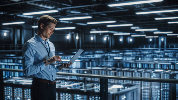 istock Portrait of IT Specialist Uses Laptop in Data Center. Server Farm Cloud Computing Facility with Male Maintenance Administrator Working. Cyber Security and Network Protection. 1336250771