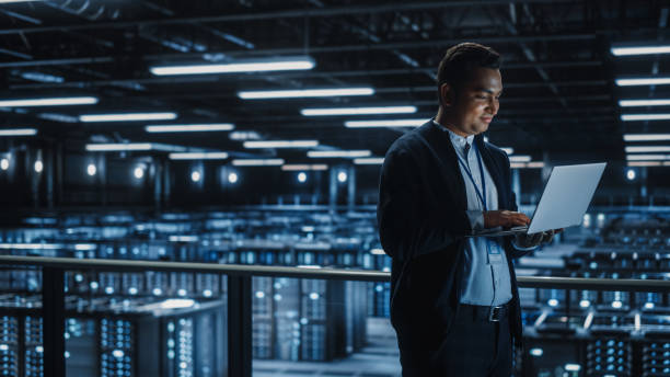 istock Portrait of IT Specialist Uses Laptop in Data Center. Server Farm Cloud Computing Facility with Male Maintenance Administrator Working. Cyber Security and Network Protection. 1336250783