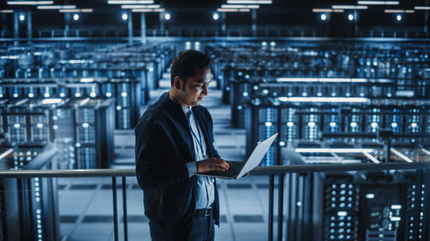 istock Portrait of IT Specialist Uses Laptop in Data Center. Server Farm Cloud Computing Facility with Male Maintenance Administrator Working. Cyber Security and Network Protection. 1336250784