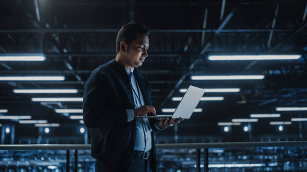 istock Portrait of IT Specialist Uses Laptop in Data Center. Server Farm Cloud Computing Facility with Male Maintenance Administrator Working. Cyber Security and Network Protection. 1336250786
