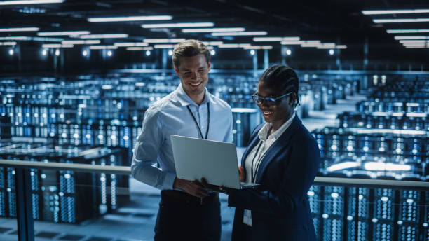 data center female system administrator i male it specialist talk, use laptop. inżynierowie technologii informatycznych pracują nad ochroną bezpieczeństwa cybernetycznego w cloud computing server farm. - women science service technology zdjęcia i obrazy z banku zdjęć