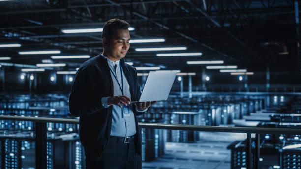 istock Portrait of IT Specialist Uses Laptop in Data Center. Server Farm Cloud Computing Facility with Male System Administrator Working. Cyber Security and Network Protection. 1336250795