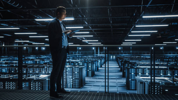 istock Portrait of IT Specialist Using Tablet Computer in Data Center. Big Server Farm Cloud Computing Facility with Male System Administrator Working. Cyber Security, Network Protection. 1336250804
