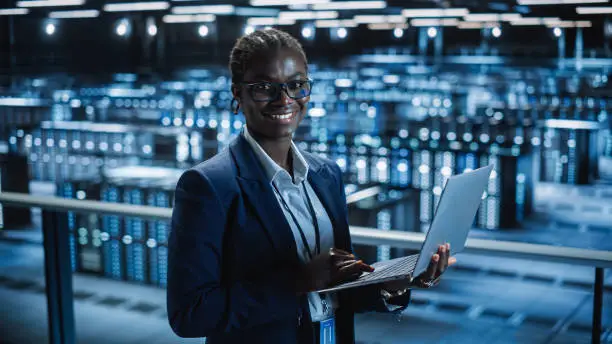 Photo of Data Center Female Programmer Using Laptop Computer, Maintenance IT Specialist. In Cloud Computing Server Farm Smiling System Administrator Working on Cyber Security for Iaas, saas, paas.