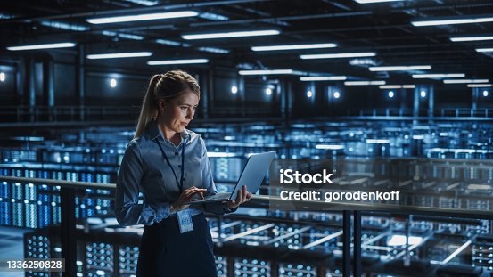 istock Data Center Female It Specialist Using Laptop. Server Farm Cloud Computing and Cyber Security Maintenance Administrator Working on Computer. Information Technology Professional. 1336250828