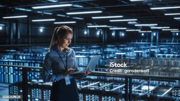 Data Center Female It Specialist Using Laptop Server Farm Cloud Computing And Cyber Security Maintenance Administrator Working On Computer Information Technology Professional Stock Photo - Download Image Now