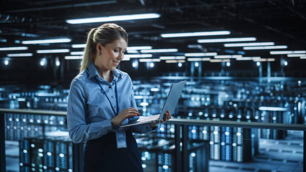 istock Portrait of IT Specialist Using Laptop in Data Center. Big Server Farm Cloud Computing Facility with Female System Administrator Monitoring. Cyber Security, Network Protection Services. 1336251054