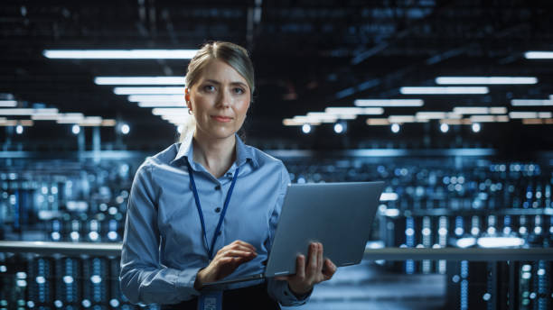 istock Portrait of Beautiful Smiling IT Specialist Using Laptop Computer in Data Center, Looking at Camera. Succesful Female e-Business Engineer Working in Big Server Farm Cloud Computing Facility. 1336251066