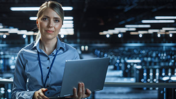 istock Portrait of Beautiful Smiling IT Specialist Using Laptop Computer in Data Center, Looking at Camera. Succesful Female e-Business Engineer Working in Big Server Farm Cloud Computing Facility. 1336251067