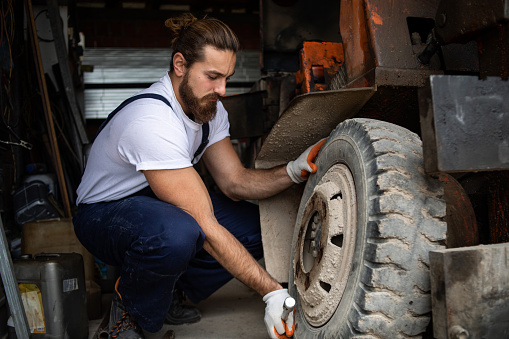 One man, a car mechanic, is in a car repair shop repairing a crane that makes it easier to work in a warehouse.