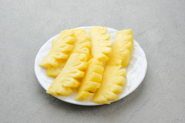 Fresh slices pineapple served in white plate, isolated on a grey background.