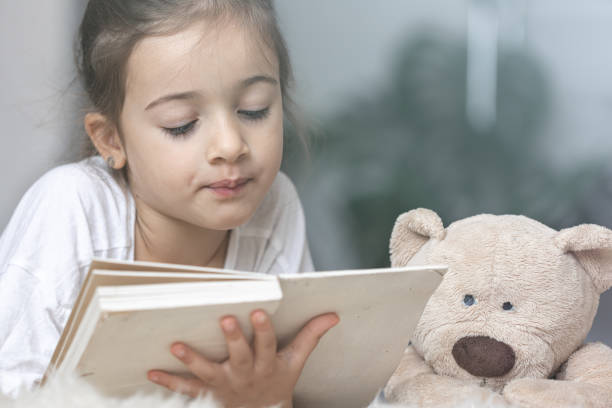 istock Little girl reads a book with a teddy bear. 1336255984