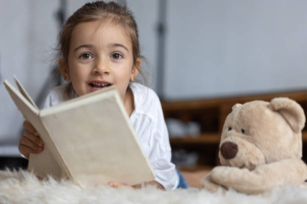 istock Little girl reads a book with a teddy bear. 1336255986