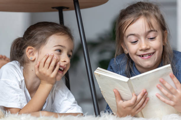 istock Two little sisters are reading a book lying on the floor on a cozy blanket. 1336255995
