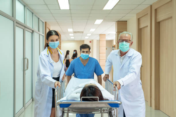médecin caucasien et infirmier asiatique déplaçant le patient blessé d’un accident sur une civière à la salle d’opération d’urgence - soins durgence photos et images de collection