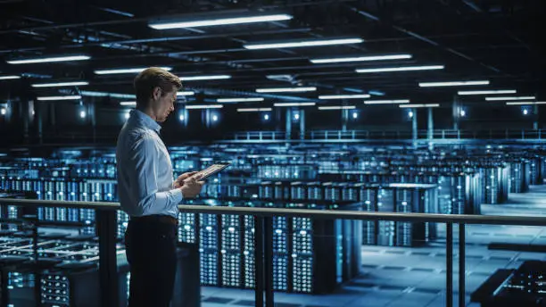 Photo of Data Center Engineer Using Digital Tablet Computer, Maintenance Specialist. High-Tech Information Protection, Cyber Security. Cloud Computing Facility. Server Farm for Iaas, saas, paas.